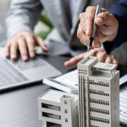 businessman holding model small building_shutterstock_2297877821 1030x385